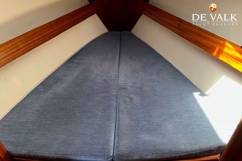 De foto toont een voorpunt van een boot met een V-vormig bed met blauwe kussens en houten afwerking. — Bavaria 31