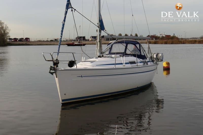 Een witte zeilboot met blauwe strepen ligt in het water, met een gele boei ernaast en land op de achtergrond. — Bavaria 31