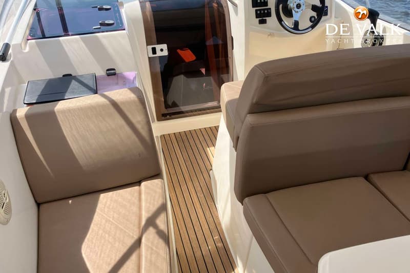 De foto toont het interieur van een boot met beige kussens, een houten vloer en een stuurwiel. — Jeanneau Leader 8