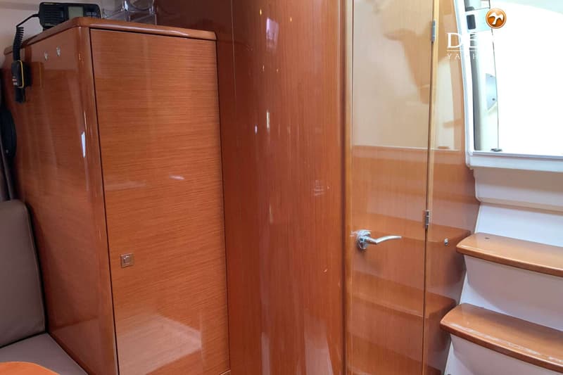 Een interieur van een boot met glanzend houten kasten, een deur met een zilveren klink en een trap met houten treden.