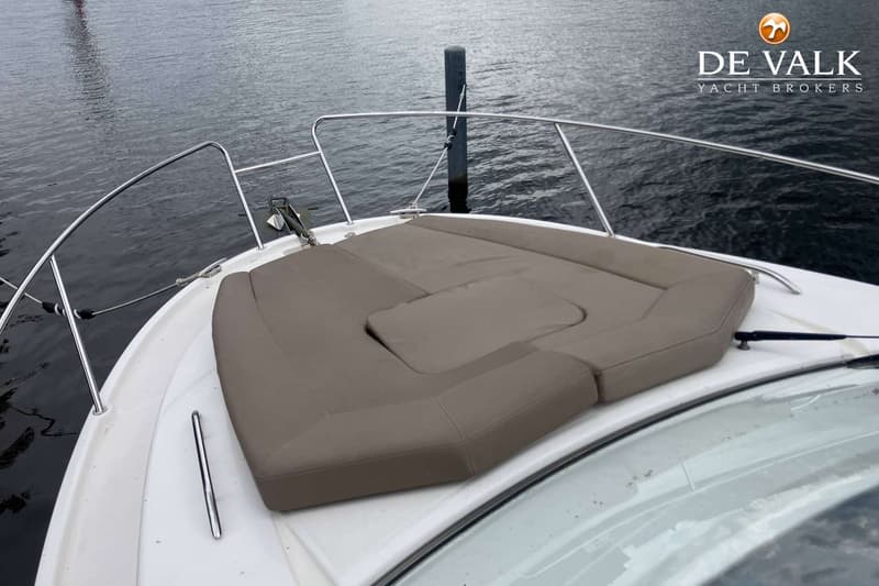 De boeg van een witte boot met beige kussens en een roestvrijstalen reling is zichtbaar, aangemeerd aan een paal.