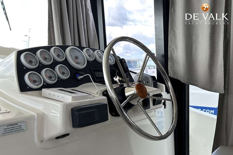 De foto toont een stuurstand met een stuurwiel, diverse meters, een waarschuwingssticker en een logo van "DE VALK YACHT…