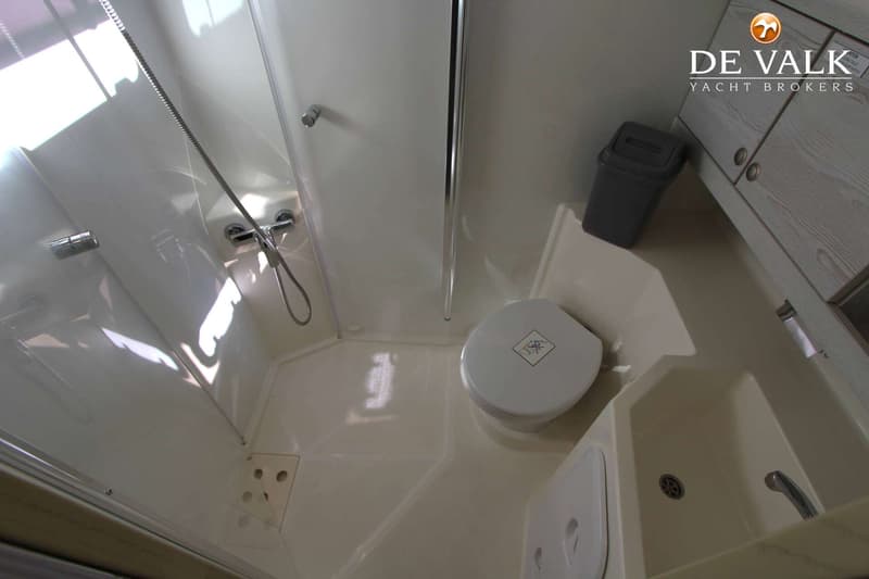 De foto toont een badkamer met een douche, toilet, wastafel en een prullenbak.