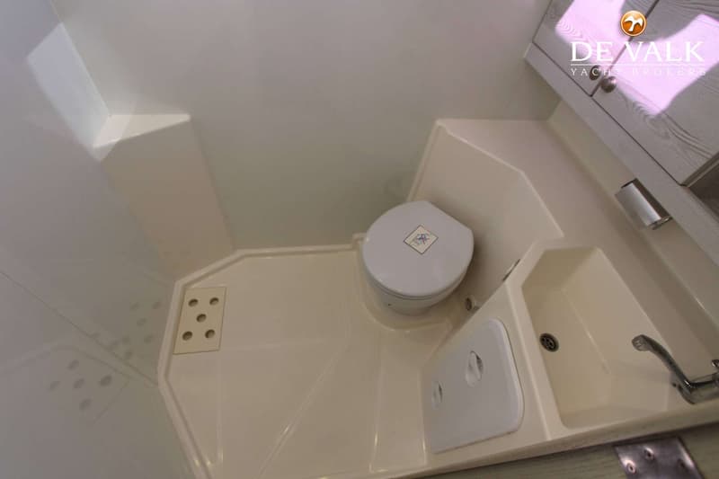 De foto toont een compacte badkamer met een toilet, een wastafel met kraan en een kastje.