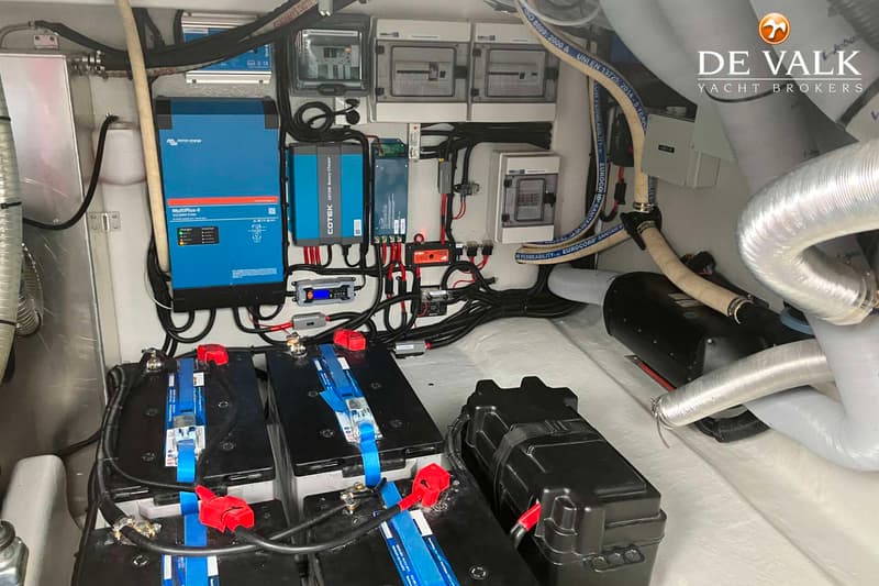 De foto toont een detail van de technische installatie van een boot, met accu's, omvormers, zekeringkasten en diverse…