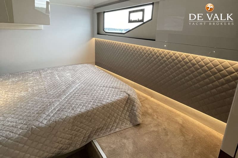 Een slaapkamer met een bed met een lichtgekleurde sprei, een gewatteerd hoofdeinde met verlichting en een raam.
