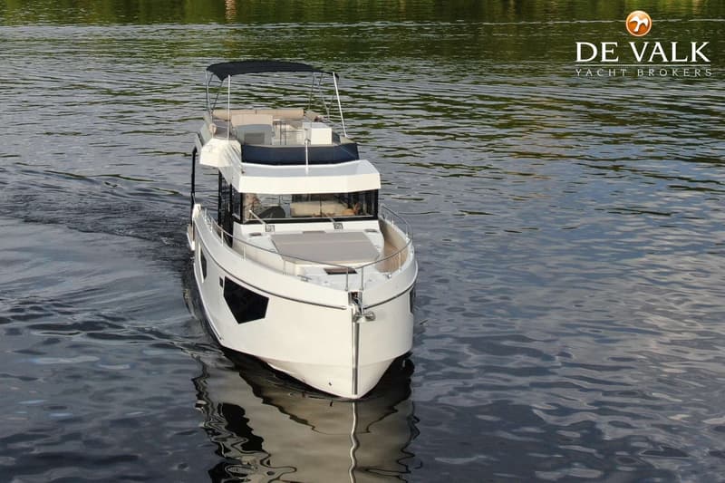 Een witte motorboot met een zwarte bimini vaart op rustig water, met een logo van "DE VALK YACHT BROKERS" rechtsboven.