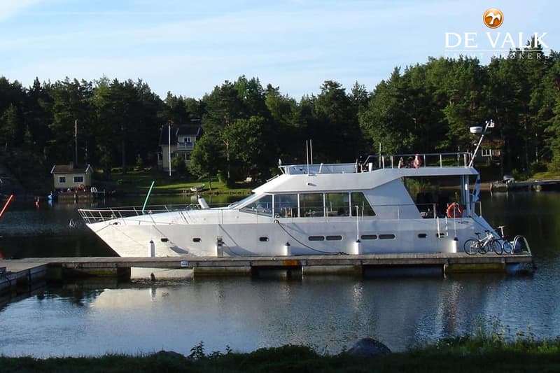 Een witte motorboot ligt afgemeerd aan een houten steiger, met bomen en huizen op de achtergrond. — One-Off Motor Yacht