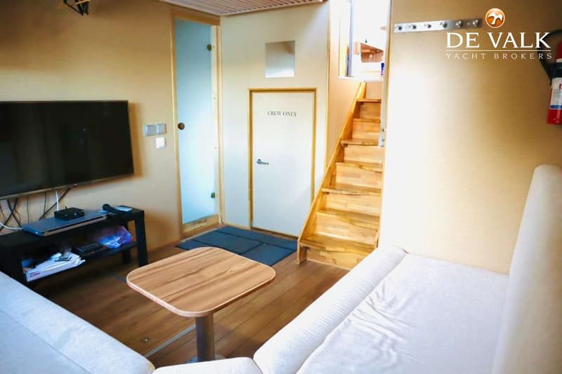 Een interieur met een bank, een salontafel, een tv-meubel met tv, een deur met "CREW ONLY" en een houten trap.