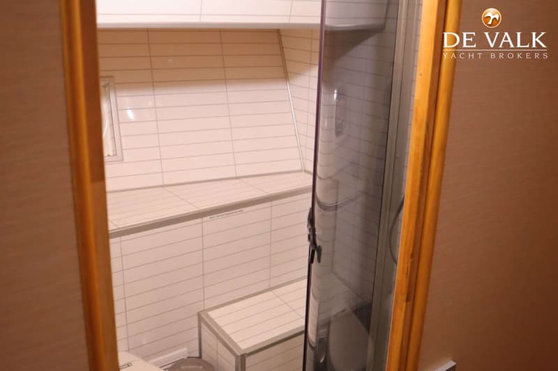 De foto toont een interieur met witte tegels, een houten deurkozijn en een glazen douchewand.