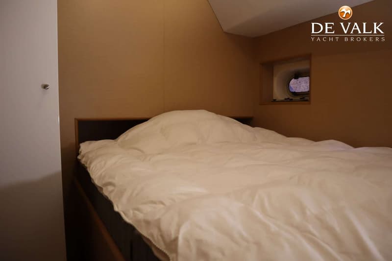 Een kajuit met een bed met wit dekbed en een patrijspoort in de bruine wand. — One-Off Motor Yacht
