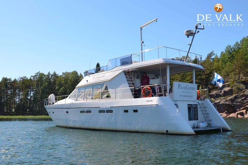 Een witte motorboot met de naam "Polar Cruiser" ligt in het water, met een Finse vlag aan de achtersteven.