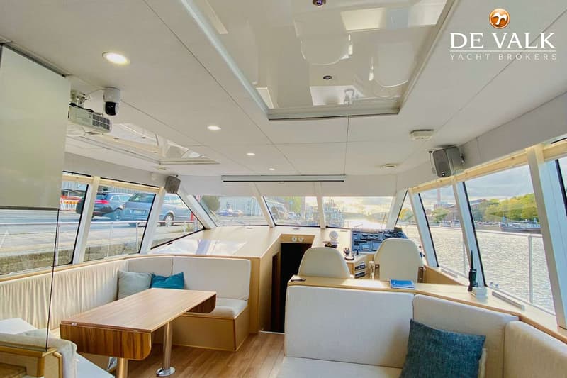 De foto toont het interieur van een boot met een zithoek, een tafel, een stuurstand en grote ramen. — One-Off Motor Yacht