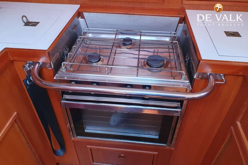 Een roestvrijstalen fornuis met drie branders en een oven, ingebouwd in een houten aanrecht met een witte afdekplaat.