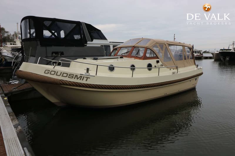 Een crèmekleurige motorboot met de naam "GOUDSMIT" op de boeg ligt aangemeerd naast een donkere boot. — Pieterse 850