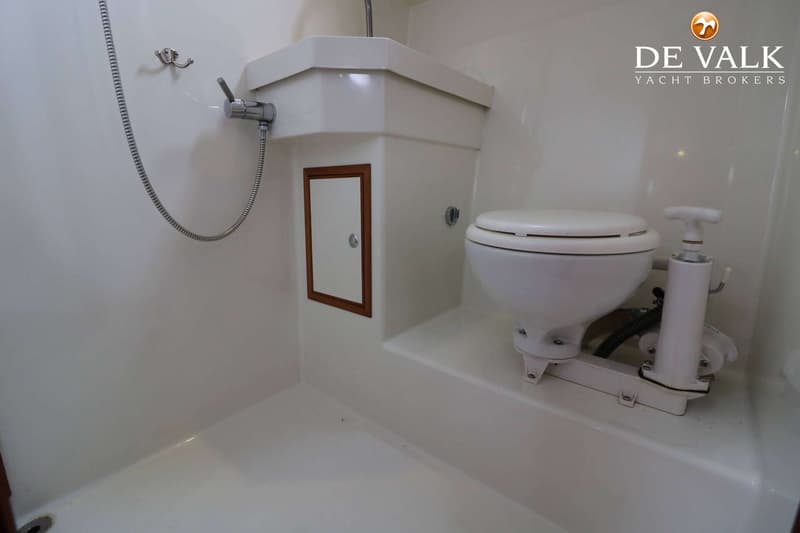 Een witte badkamer met een toilet, een wastafel met kraan en een douchekop aan de muur.