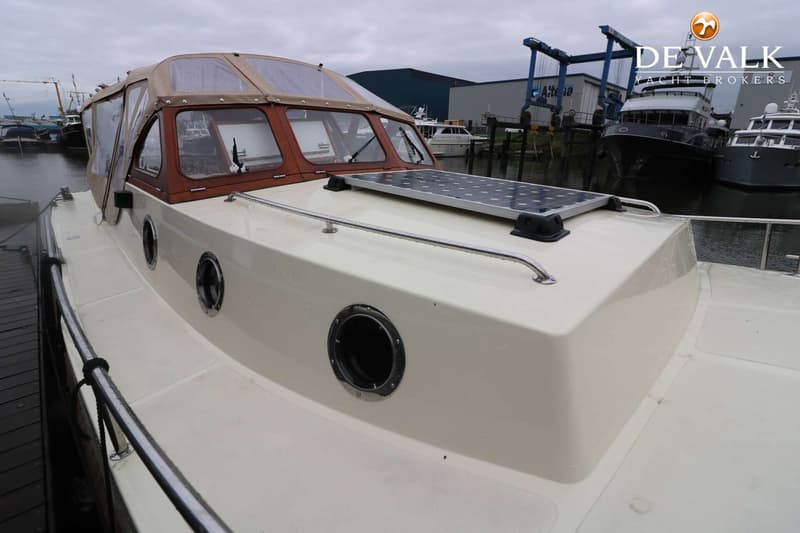 Een boot met een beige kap en houten raamkozijnen ligt in een haven met een zonnepaneel op het voordek. — Pieterse 850