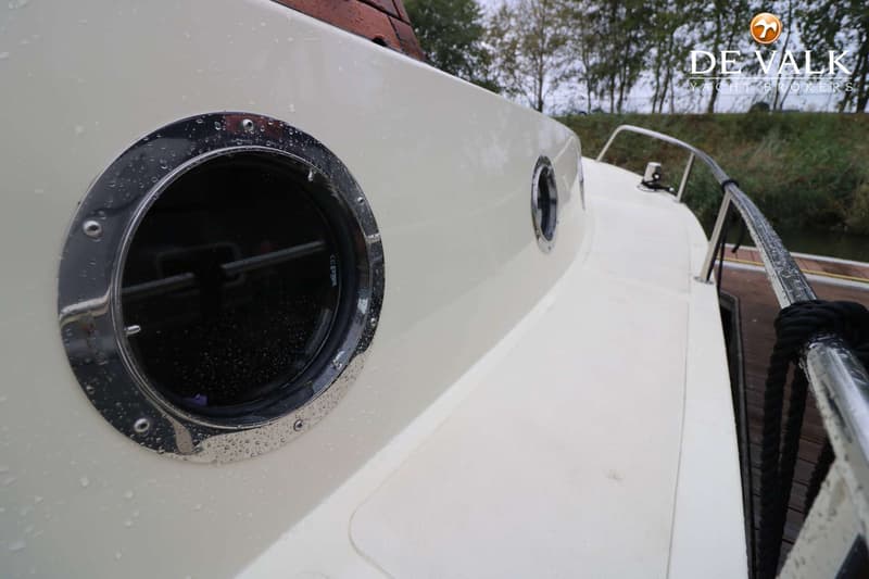 Een close-up van de zijkant van een boot met twee ronde patrijspoorten, waarvan één groot en één kleiner, en een reling.