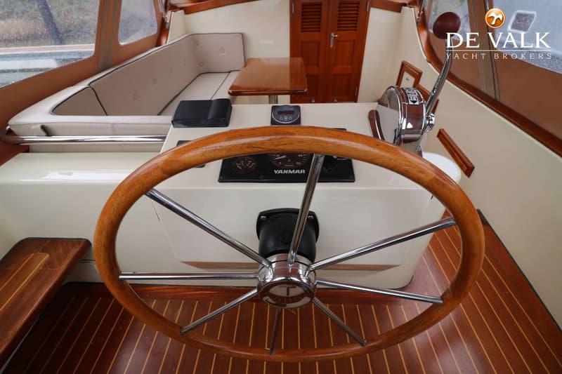 Een houten stuurwiel met chromen spaken en een Yanmar-paneel zijn zichtbaar in de cockpit van een boot. — Pieterse 850