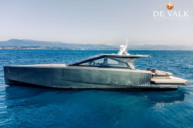 Een donkergrijze motorboot met een gestroomlijnd ontwerp ligt op helderblauw water, met bergen op de achtergrond.