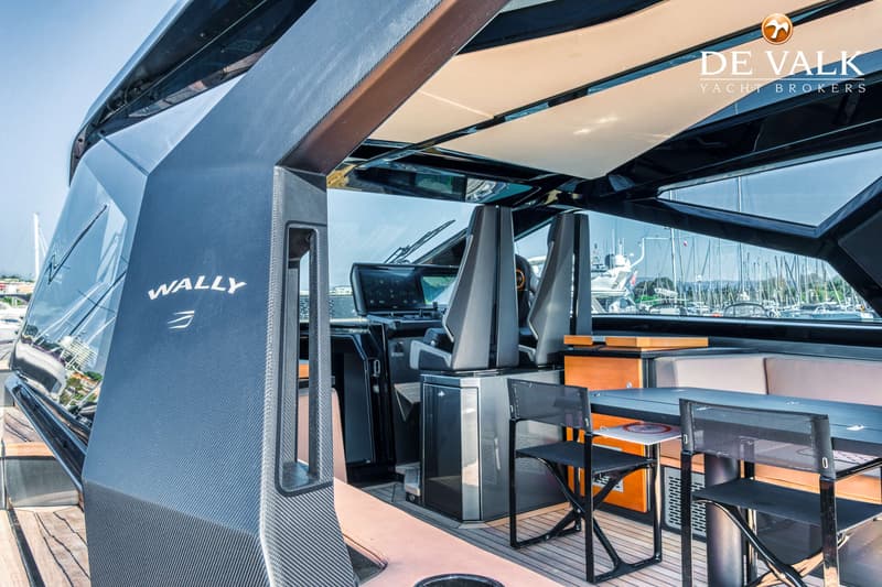 De foto toont het interieur van een Wally-jacht met stuurstand, zitplaatsen en een tafel, met uitzicht op een jachthaven.