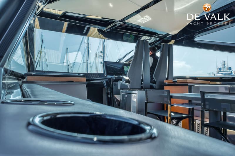 Een interieur van een boot met een stuurstand, stoelen, een tafel en uitzicht op andere boten. — Wally WallyPower58