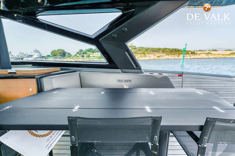 Een bootinterieur met een zwarte tafel en stoelen, met uitzicht op water en een groene boei.