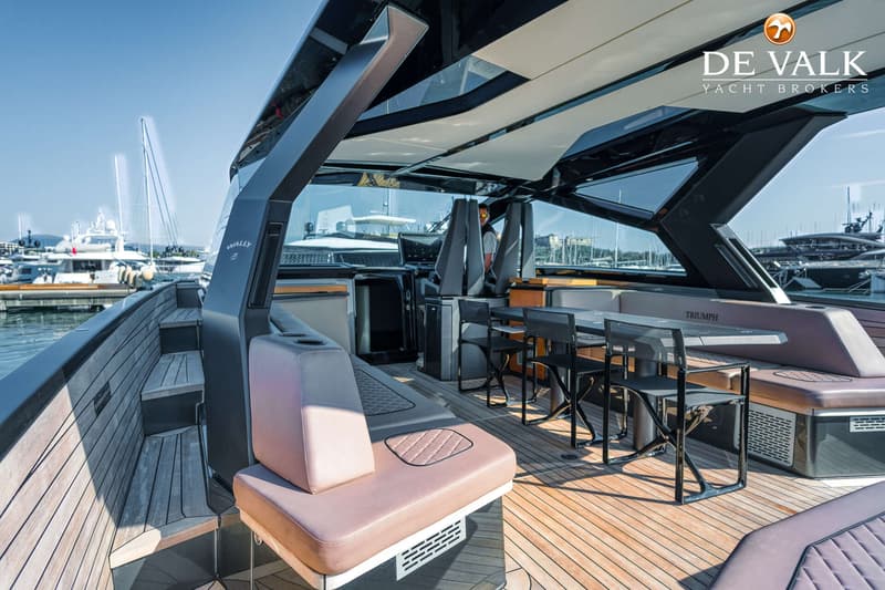 Een luxe jacht met een houten dek, zitplaatsen, een tafel en een stuurstand, afgemeerd in een haven. — Wally WallyPower58