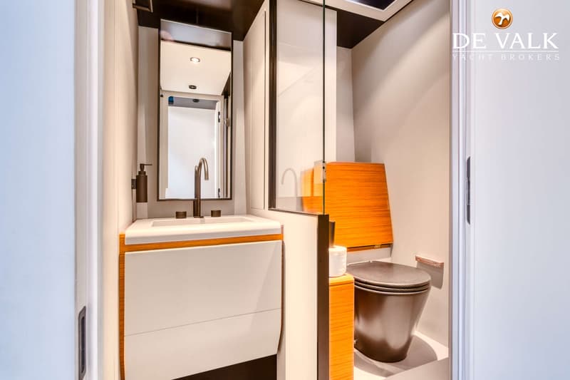 Een badkamer met een wastafel, spiegel, toilet en een glazen douchewand is zichtbaar.
