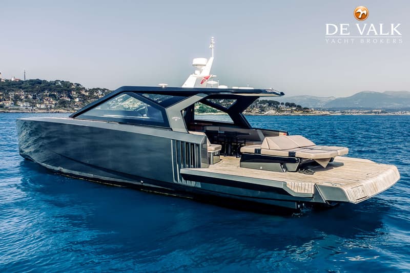 Een donkergrijze motorboot met een houten dek en een zonnebed ligt op helderblauw water. — Wally WallyPower58