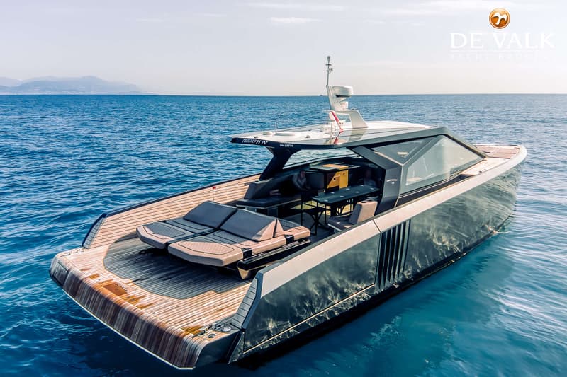 Een moderne motorboot met houten dek en donkere romp ligt op helderblauw water, met bergen op de achtergrond.