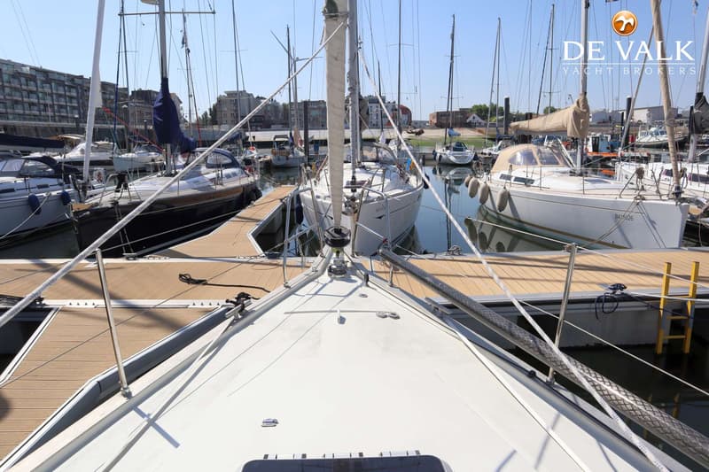 De foto toont het voordek van een witte zeilboot, met uitzicht op een jachthaven vol met andere boten en aanlegsteigers.