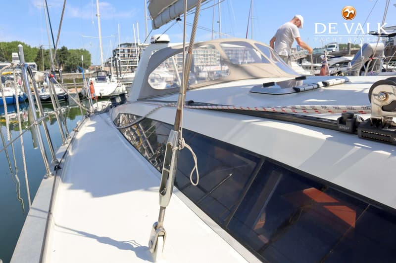 Een witte zeilboot met een beige buiskap en een man op het dek, liggend in een haven met andere boten. — Berckemeyer 43