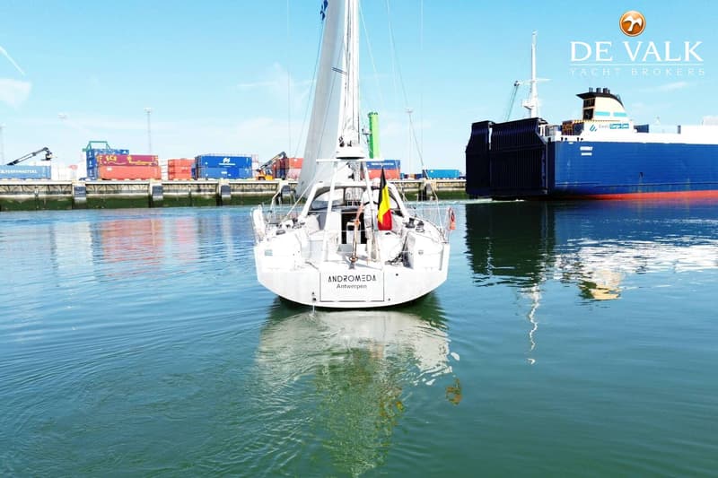 Een witte zeilboot met de naam "ANDROMEDA Antwerpen" vaart op water, met een Belgische vlag aan de achtersteven.