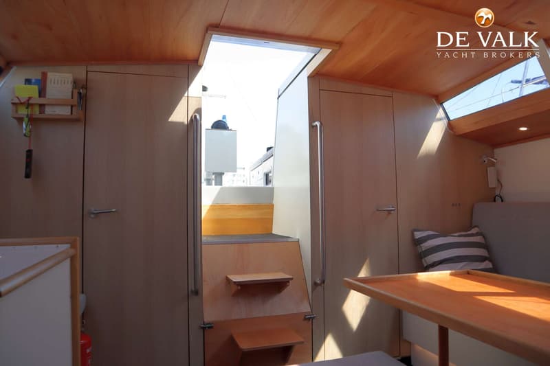 De foto toont het interieur van een boot met houten wanden en plafond, een trap naar buiten, en een zithoek met tafel.