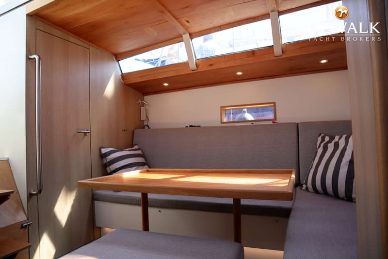 Een houten tafel met banken en kussens in een kajuit met houten plafond en ramen. — Berckemeyer 43