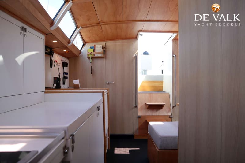 De foto toont het interieur van een boot met houten wanden en plafond, een wit aanrechtblad en een trap naar buiten.
