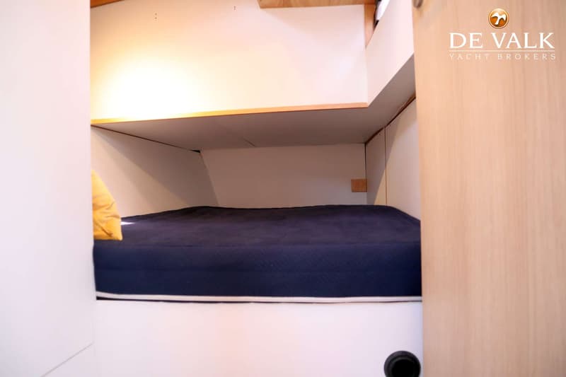 Een kajuit met een donkerblauw matras en een geel kussen, omringd door witte en houten panelen. — Berckemeyer 43