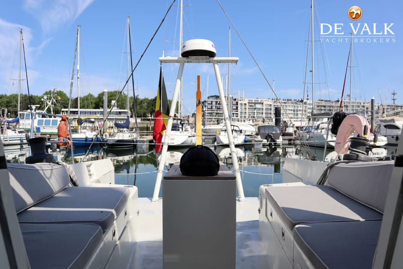 Een achterdek van een boot met twee zitbanken en een centrale console, uitkijkend over een jachthaven met andere boten.