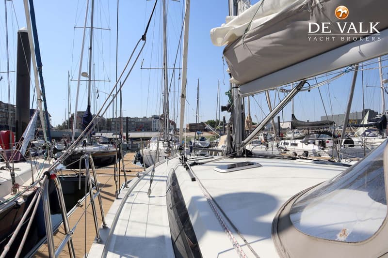 Een zeilboot ligt in een jachthaven, met een deel van het dek en de mast zichtbaar, omringd door andere boten.