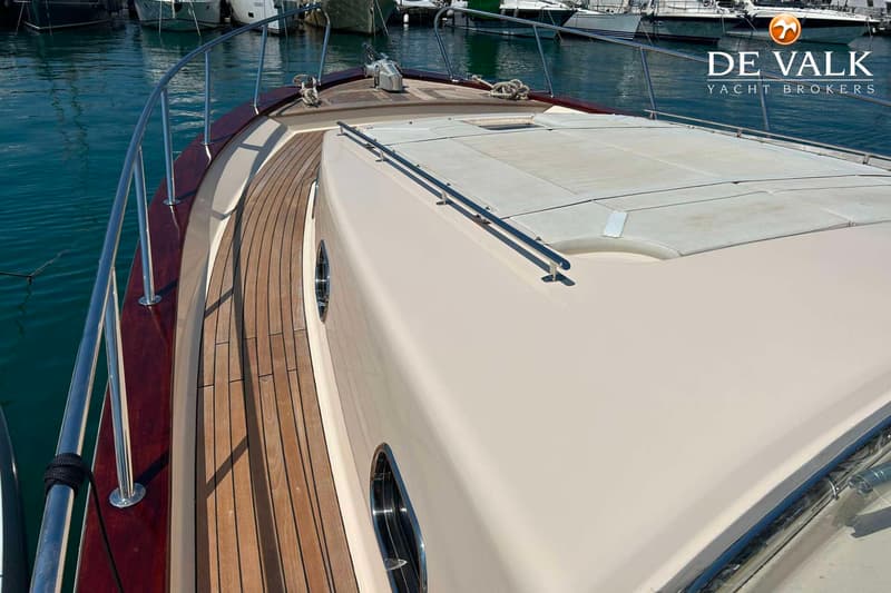 Een bovenaanzicht van de boeg van een boot met een teakhouten dek, patrijspoorten en een reling. — Apreamare 12 Cabinato