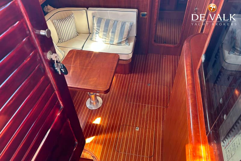 Een interieur van een boot met houten vloer en wanden, een bank met kussens en een tafel. — Apreamare 12 Cabinato