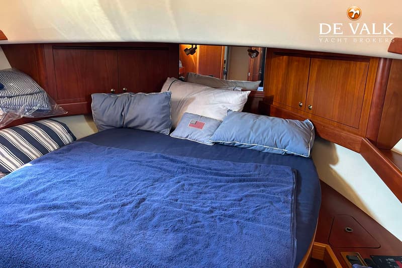 Een kajuit met een bed, blauw beddengoed, kussens en houten kasten. — Apreamare 12 Cabinato