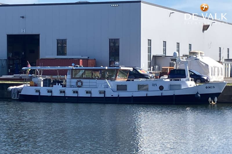 Een witte boot met een donkerblauwe romp ligt in het water voor een groot grijs gebouw. — Luxe motor 22 m