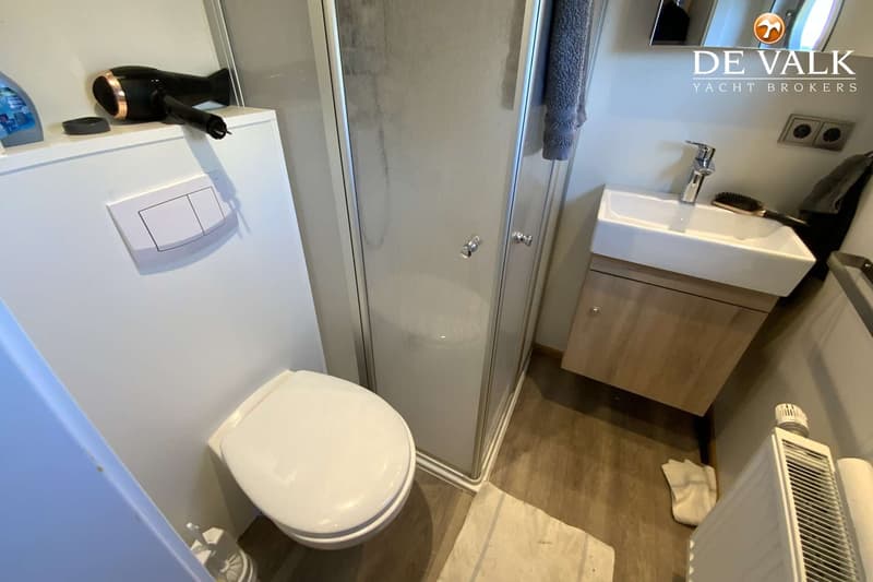 De foto toont een badkamer met een toilet, een douchecabine, een wastafel met een houten onderkast en een radiator.