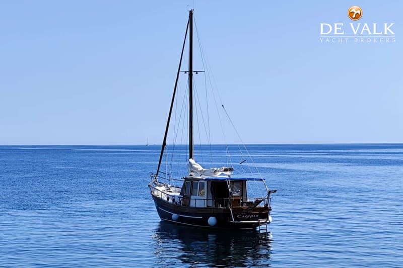 Een donkerblauwe zeilboot met de naam "Calypso" ligt op helderblauw water onder een strakblauwe lucht.