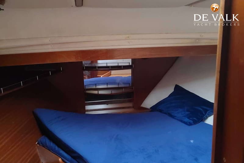 Een kajuit met een blauw matras en een blauw kussen, met een spiegel aan de zijkant en houten afwerking.