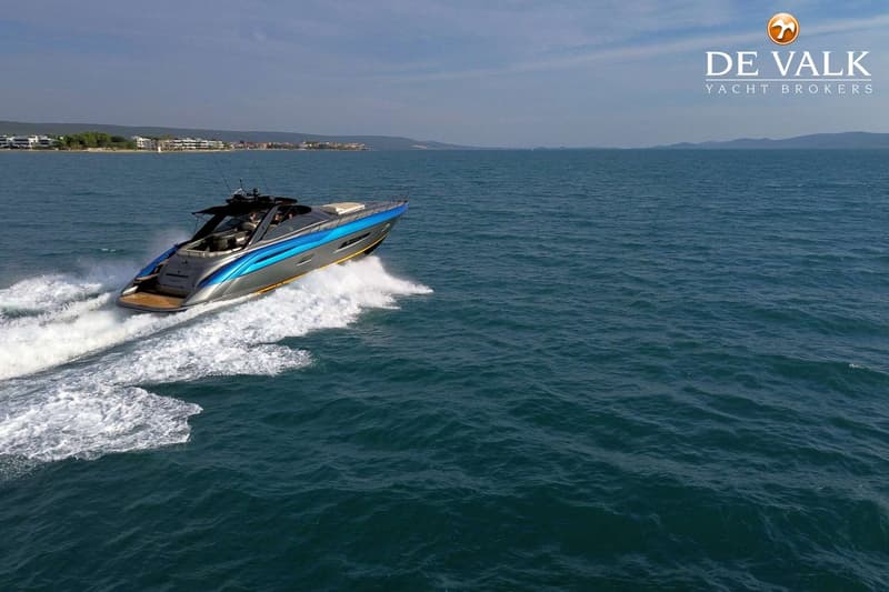 Een grijze en blauwe motorboot vaart snel over het water, met een kustlijn en bergen op de achtergrond.