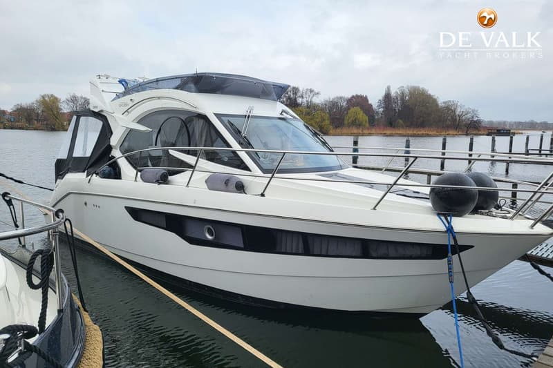 Een witte motorboot met een donkerblauwe kap en ramen, afgemeerd aan een steiger met een waterig landschap op de achtergrond.
