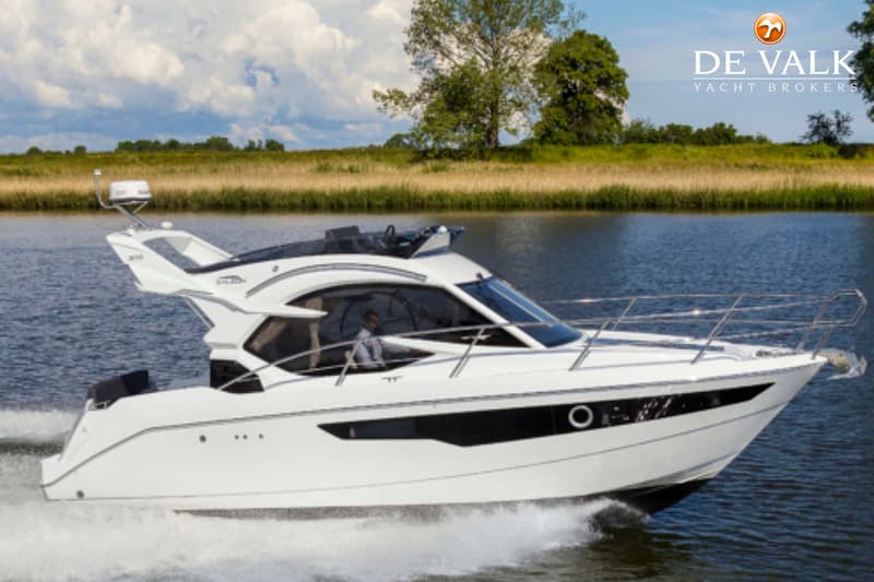 Een witte motorboot met zwarte ramen vaart over water, met een man aan het roer, langs een groene oever. — Galeon 300 Fly
